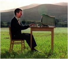 A man in a field sits at a computer workstation