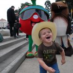 A child in a cowboy hat runs from costumed mascots at Ag Day