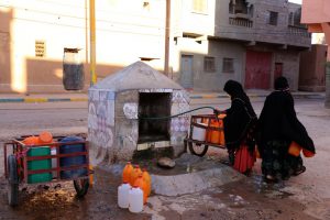 Moroccan women fill up containers with water from a hose